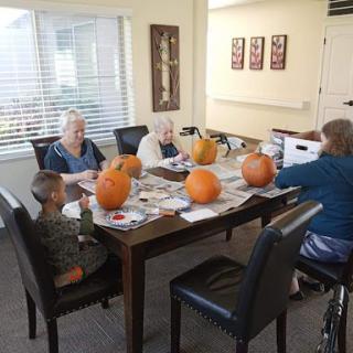 A group of adults and a child enjoying an indoor pumpkin carving activity.