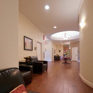 A well-lit hallway with wooden flooring, featuring a seating area and decorative artwork.