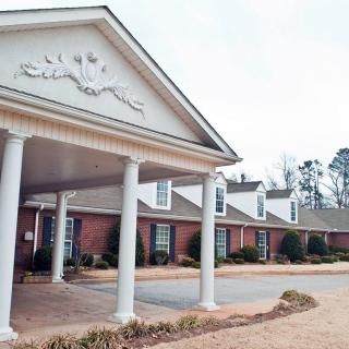 Front view of a brick building with white columns and a landscaped entrance.