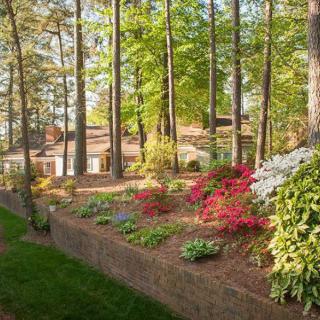 A landscaped garden featuring colorful flowers and tall trees surrounding a house.