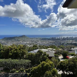 A scenic view overlooking a city with the ocean in the background and clouds scattered across a blue sky.