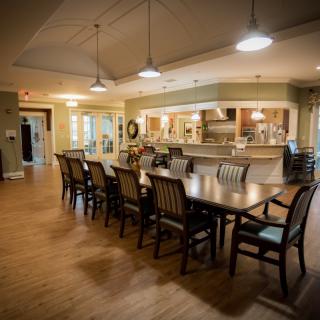 A spacious dining room with a long wooden table and chairs, adjacent to a kitchen area.