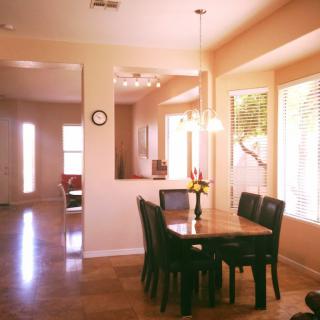 A well-lit dining area with a wooden table and chairs, featuring large windows and elegant lighting.