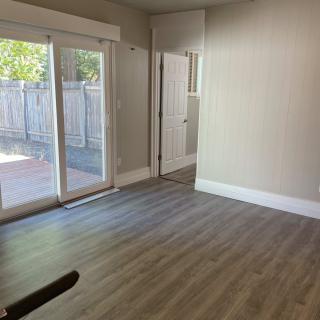 An empty room with modern flooring, large windows, and a sliding glass door letting in natural light.