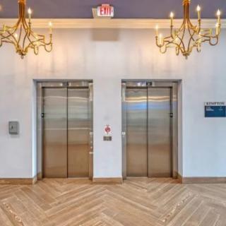 A modern lobby featuring two elevators, elegant chandeliers, and stylish wooden flooring.
