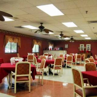 An empty dining room with tables covered in red tablecloths and chairs neatly arranged, featuring ceiling fans and ample lighting.