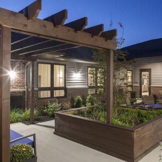 A modern outdoor patio with a wooden pergola and garden at dusk.