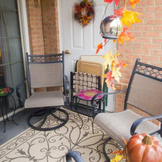 A cozy patio with autumn-themed decorations, featuring chairs and a pumpkin.