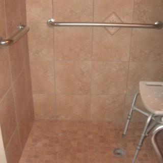 An accessible bathroom shower with a grab bar and a shower chair.