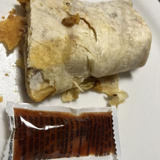 A partially unwrapped burrito on a plate with a sauce packet.