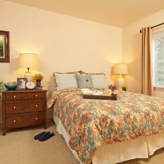 A cozy bedroom with a bed, nightstands, lamps, and a window letting in natural light.