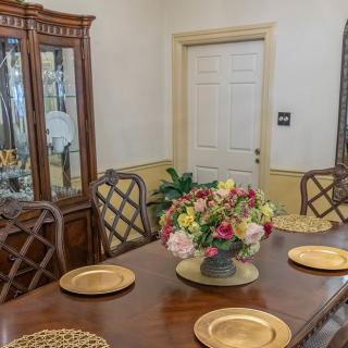 A dining room with a wooden table set for a meal, featuring a central flower arrangement and surrounded by elegant chairs.