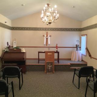 A serene chapel interior featuring an altar, chandelier, and seating arrangements.