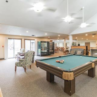 A spacious game room featuring a pool table with comfortable seating and bright lighting.