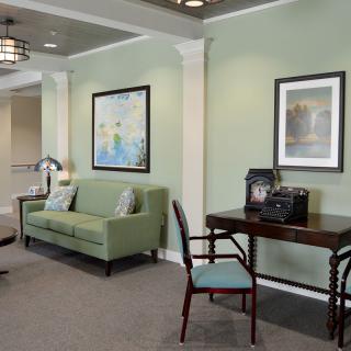 A cozy living room with a green sofa, desk, and artwork on the walls.