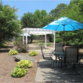 A tranquil garden patio with a table, chairs, and a blue umbrella.