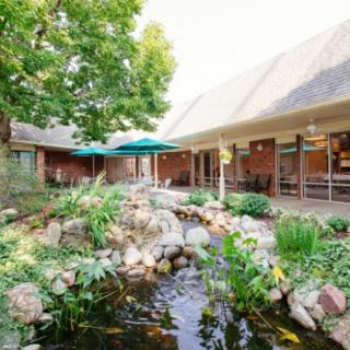 A serene outdoor garden with a pond and surrounding landscaping, adjacent to a building with patio umbrellas.