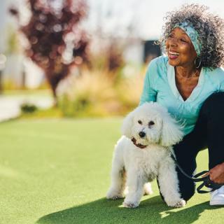 A woman enjoys a sunny day in the park with her poodle.