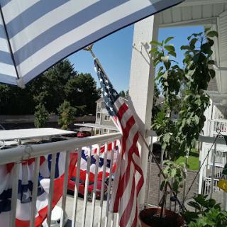A cozy balcony setup featuring an American flag and a striped umbrella, perfect for enjoying sunny days.