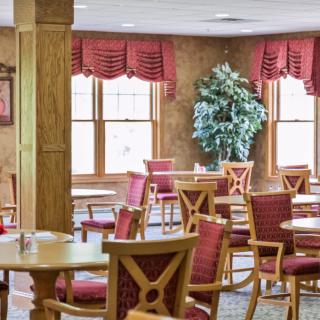 An inviting dining area with red cushioned chairs, wooden tables, and natural light from large windows.