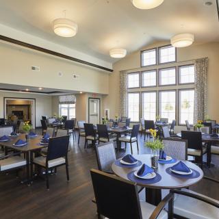 A well-lit dining area with neatly arranged tables and chairs, featuring large windows and tasteful decor.