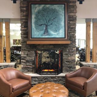 A cozy seating area with a stone fireplace and leather armchairs, adorned by a tree painting above the mantel.