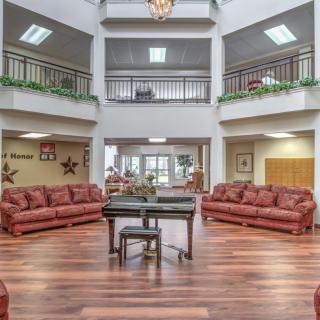 A spacious living room with red sofas, a wooden floor, and a central chandelier under an atrium.
