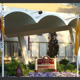 The image depicts the entrance to a hotel with unique architectural design and a welcoming sign surrounded by flags and flowers.
