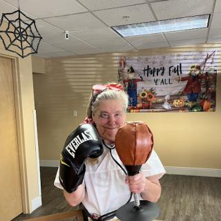 A cheerful individual dressed in a boxing-themed costume, ready for some fun with gloves and a punching bag, amidst a festive decorated background.