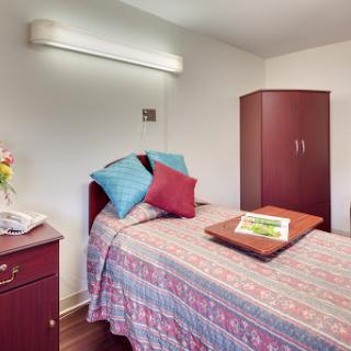 A cozy bedroom featuring a neatly made bed, colorful pillows, and a wooden wardrobe.