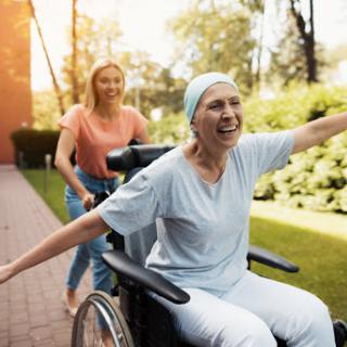 A caregiver joyfully pushes a woman in a wheelchair through a beautiful outdoor setting, showcasing companionship and support.