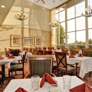 A beautifully lit restaurant dining room with elegant table settings and large windows.
