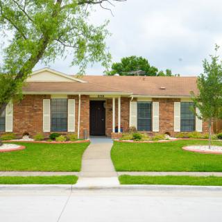 A suburban brick house with a neatly maintained lawn and trees.