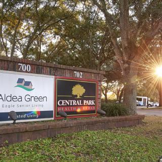 Entrance signs for Aldea Green and Central Park apartment complexes with sunlight filtering through the trees.