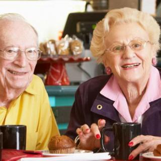An elderly couple enjoying coffee and a muffin together at a cafe.