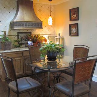 A cozy kitchen dining area with a glass-top table surrounded by four chairs, decorated with plants and warm lighting.