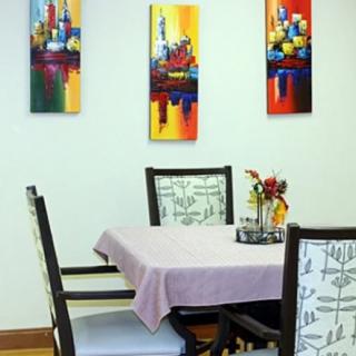 A dining room with a table covered by a purple tablecloth, surrounded by chairs and adorned with colorful artwork on the walls.