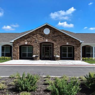 A modern brick building under a bright blue sky with white clouds, surrounded by a driveway and landscaping.