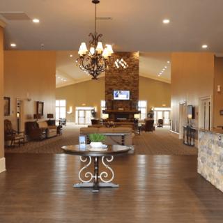 A spacious and modern lobby featuring a central table, chandelier, stone fireplace, and wood flooring.