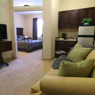 A cozy apartment interior featuring a living area with a sofa and TV, leading into a bedroom and kitchenette.