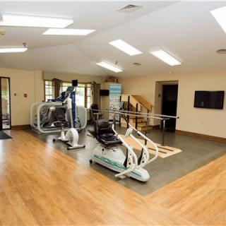 A well-lit gym with various exercise equipment and wooden flooring.