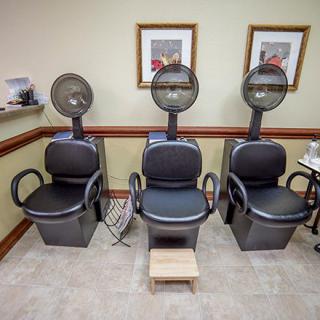 Three salon chairs with hair dryers lined up in a hair salon.