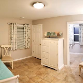 A cozy bedroom with a white dresser, chair, and patterned curtains.