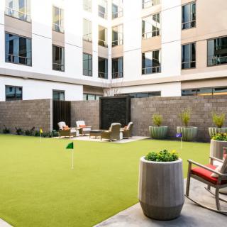 A modern courtyard with artificial turf, surrounded by a building, featuring lounge chairs and potted plants.