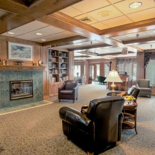A cozy living room with wood paneling, featuring a fireplace, comfortable armchairs, bookshelves, and warm lighting.