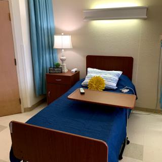 A well-lit patient room featuring a hospital bed, bedside lamp, and decorative touches.