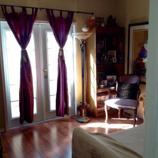A cozy living room with purple curtains, a chair, and a lamp beside French doors.