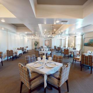 A spacious and elegantly decorated dining room with tables set for guests, featuring chandeliers and a warm ambiance.