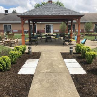 A well-maintained garden with a central pathway leading to a gazebo, surrounded by lush plants and outdoor seating.
