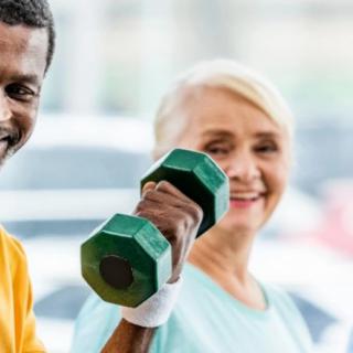 Two individuals smiling and exercising with dumbbells.